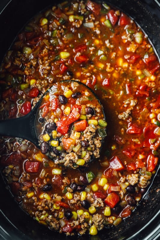 overhead view of a ladle scooping taco soup from a crockpot.