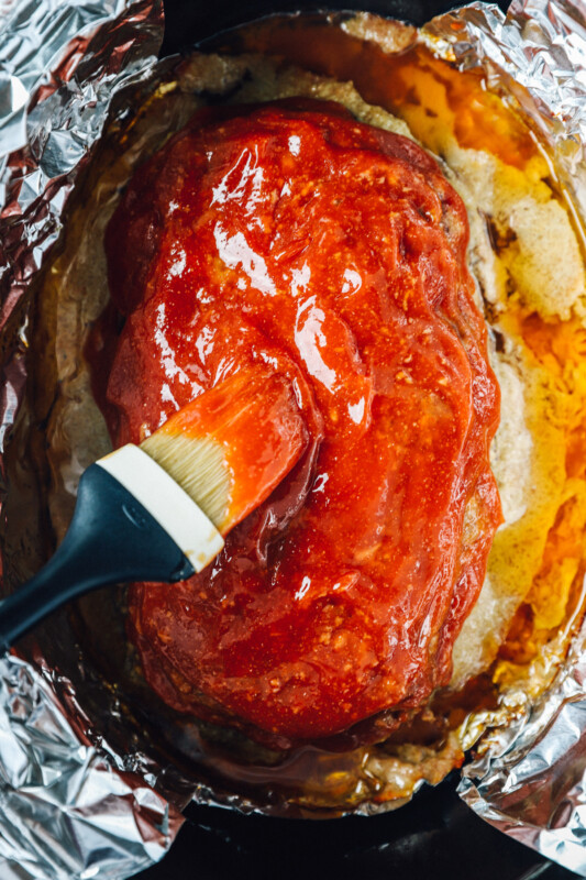 overhead view of glaze being brushed onto crockpot meatloaf in a crockpot.