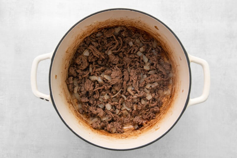 overhead view of ground beef and onions in a white dutch oven.