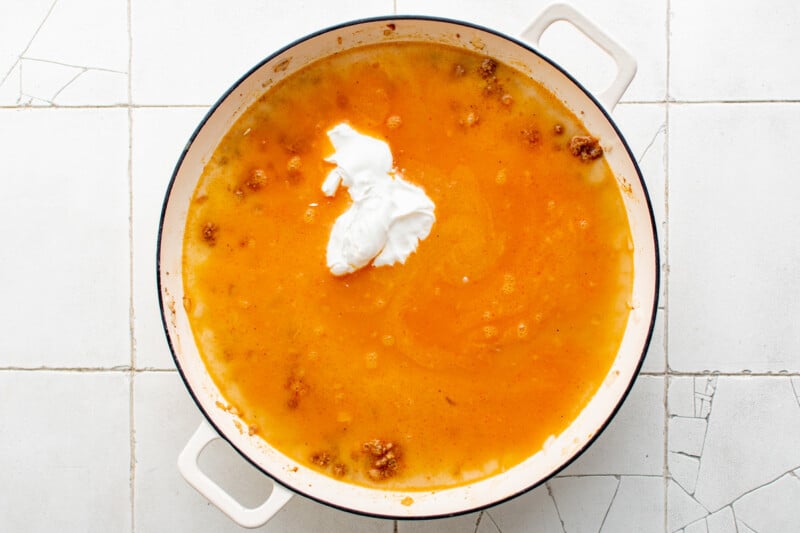 overhead view of broth, milk, and sour cream added to cooked ground beef in a white pan.