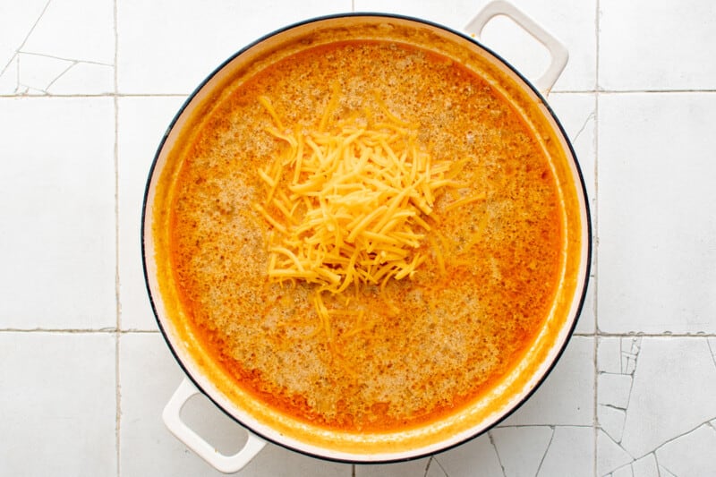 overhead view of cheese added to hamburger helper in a white pan.