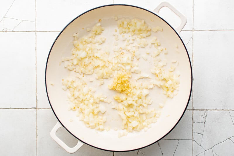 overhead view of onion and garlic cooking in a white pan.