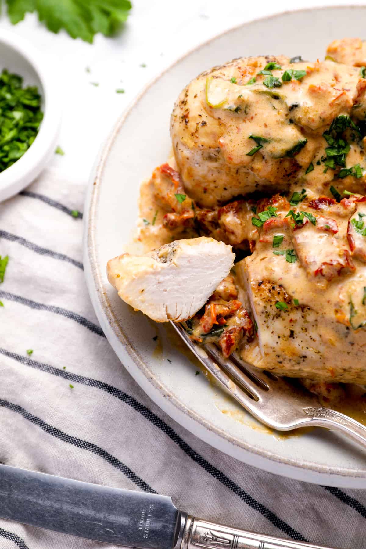 Une fourche de poulet qui repose sur une assiette avec une casserole immédiate poulet toscan dans une sauce à l'ail crémeuse