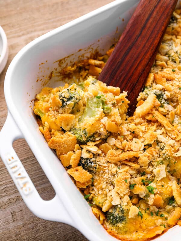 broccoli cheese casserole in a white baking pan with a wooden spoon.