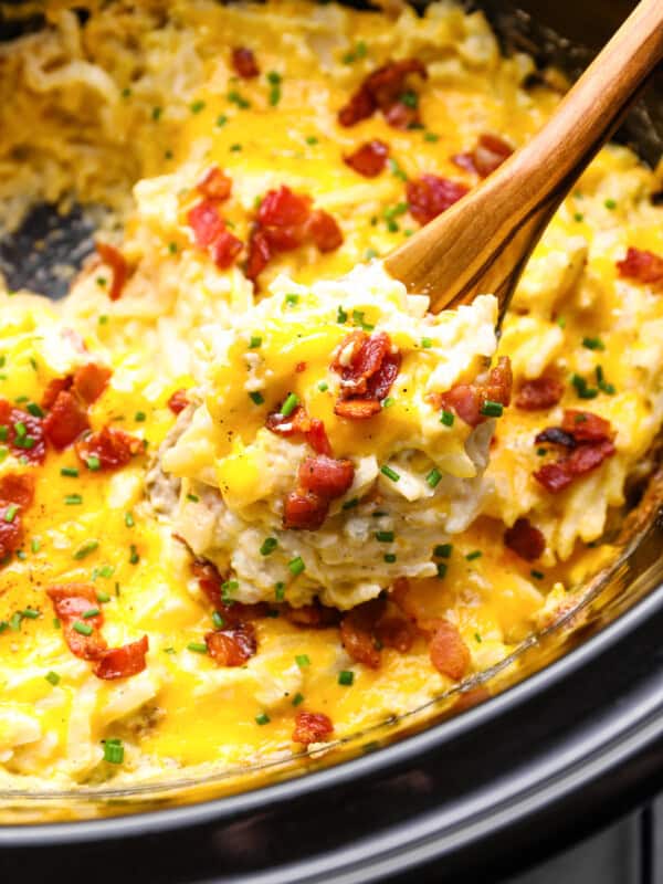 a spoon lifting a scoop of crockpot cheesy hashbrown potatoes out of a crockpot.