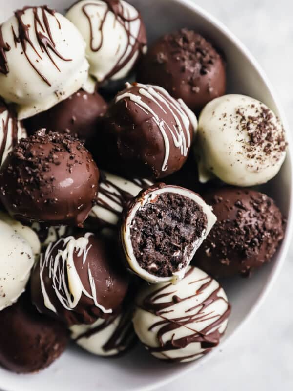 a bitten oreo ball resting on a pile of oreo balls in a white bowl.