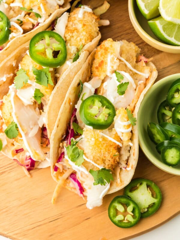 overhead view of 3 air fryer fish tacos on a wooden cutting board with sliced jalapeños.