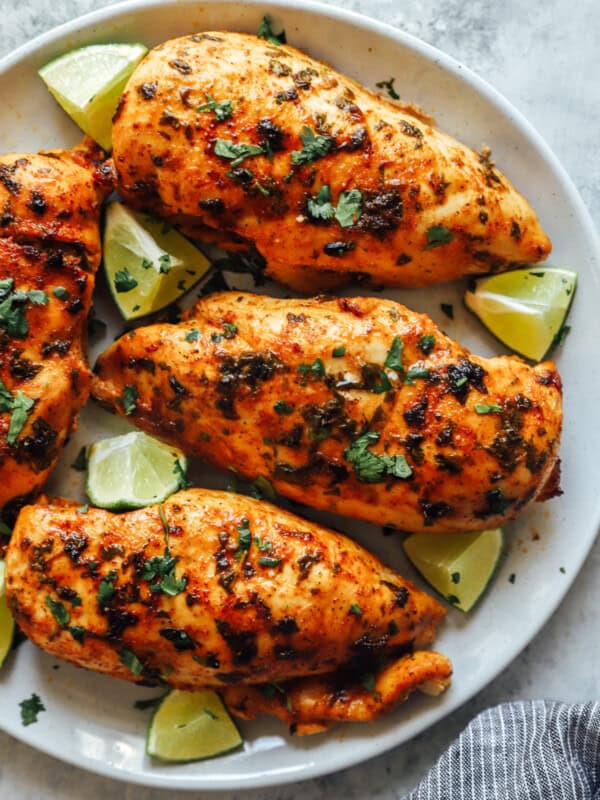 partial overhead view of 4 cilantro lime chicken breasts surrounded by lime wedges on a white plate.