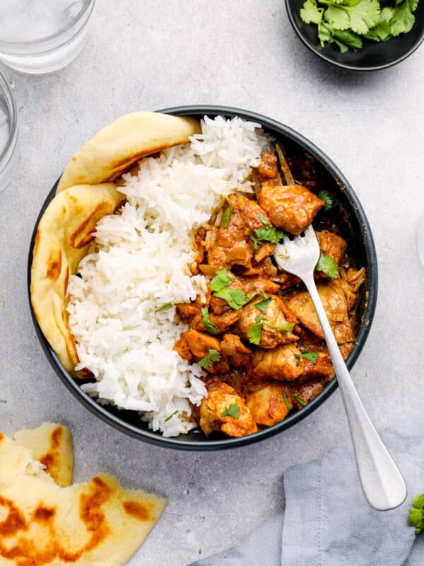 overhead view of crockpot chicken tikka masala with rice and naan in a black bowl with a fork.