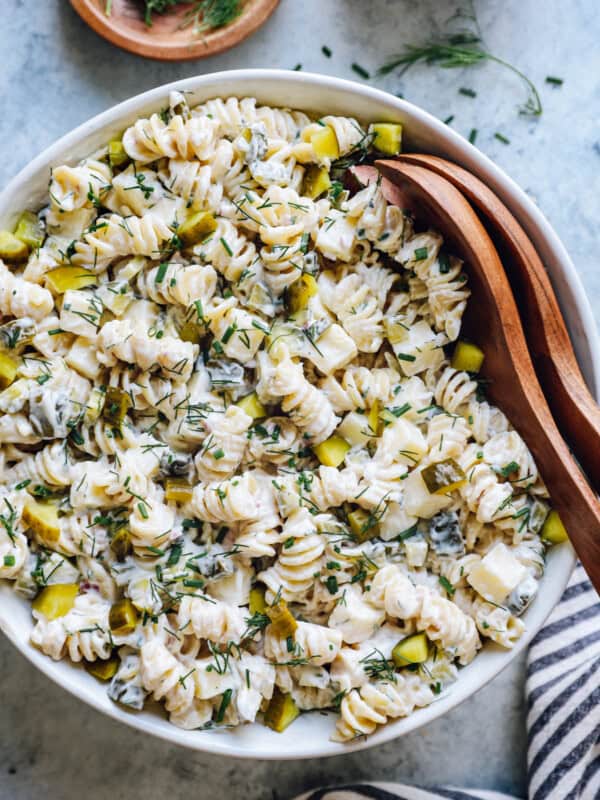 overhead view of dill pickle pasta salad in a white serving bowl with wooden salad tongs.