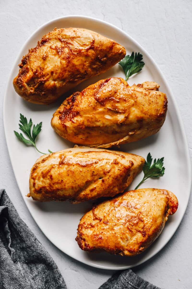 overhead view of marinated baked chicken breasts on a white oval serving platter.