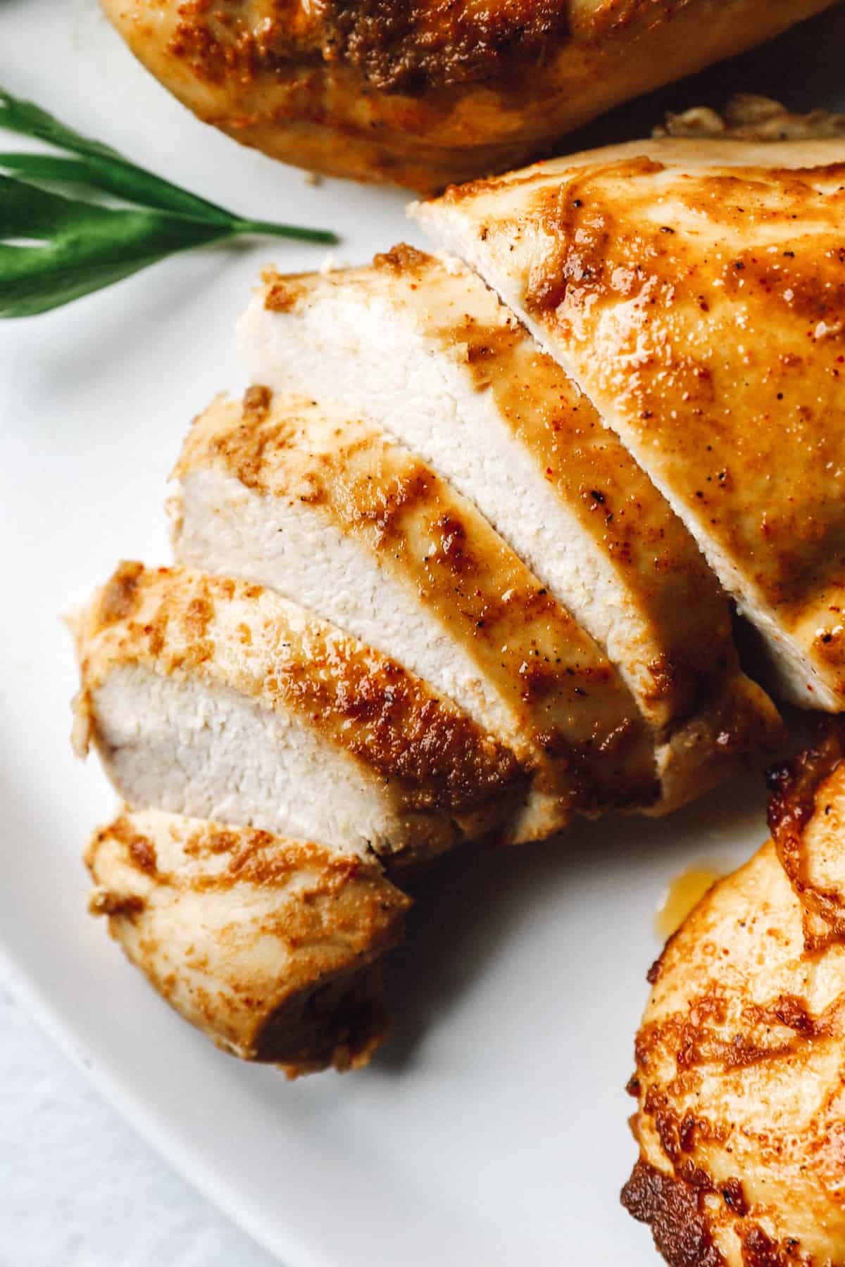 close up of a partially sliced baked marinated chicken breast on a white platter.