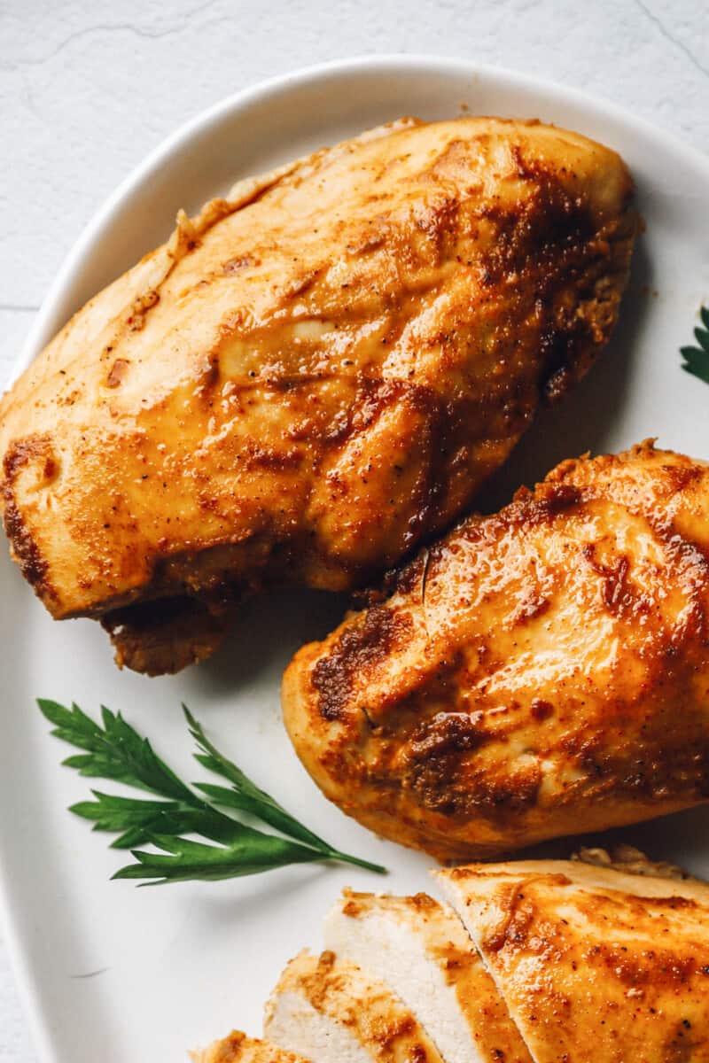 partial view of baked marinated chicken breasts on a white oval serving platter.