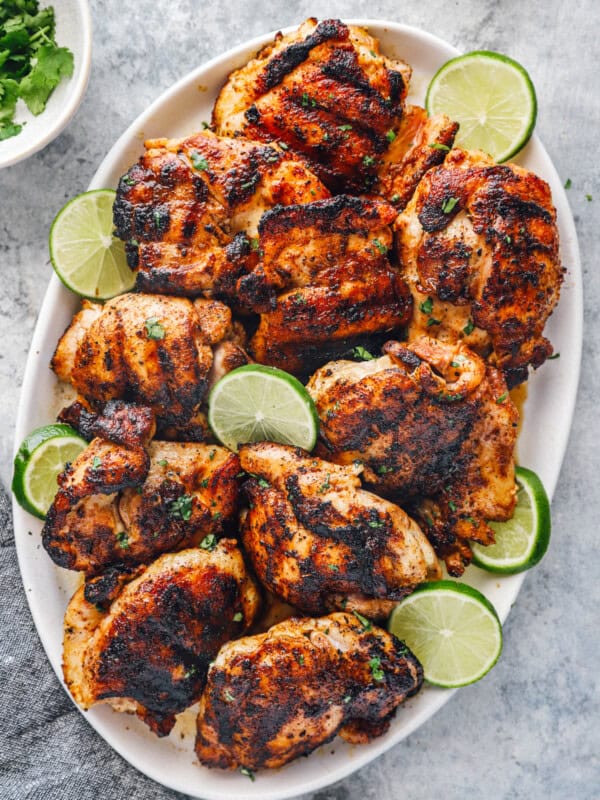 overhead view of grilled chicken thighs on a white oval serving platter with lime slices.