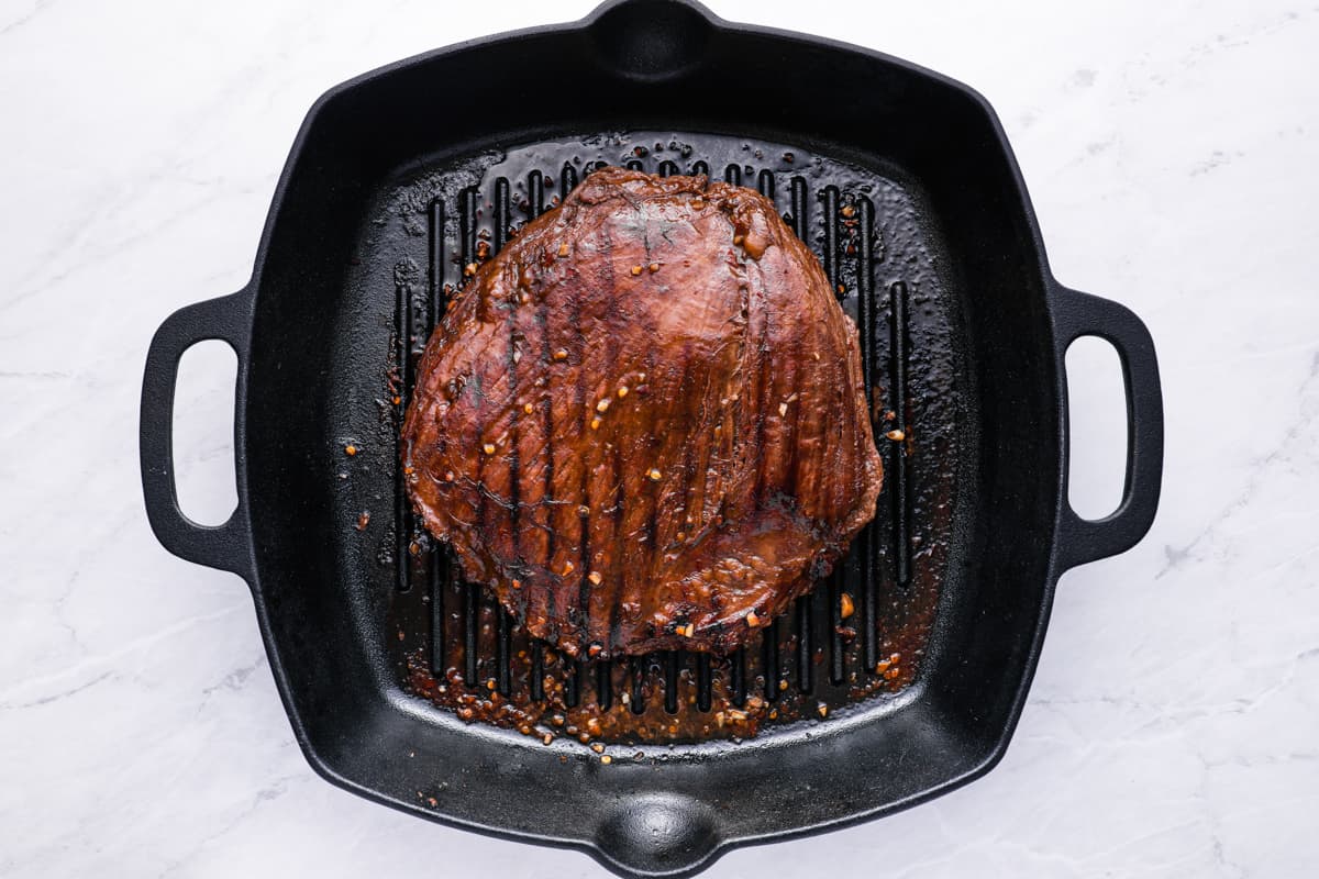 overhead view of flank steak cooking in a cast iron grill pan.