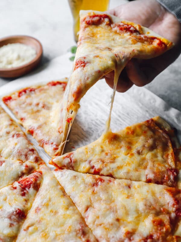 a hand grabbing a slice of new york pizza from a cut pie.