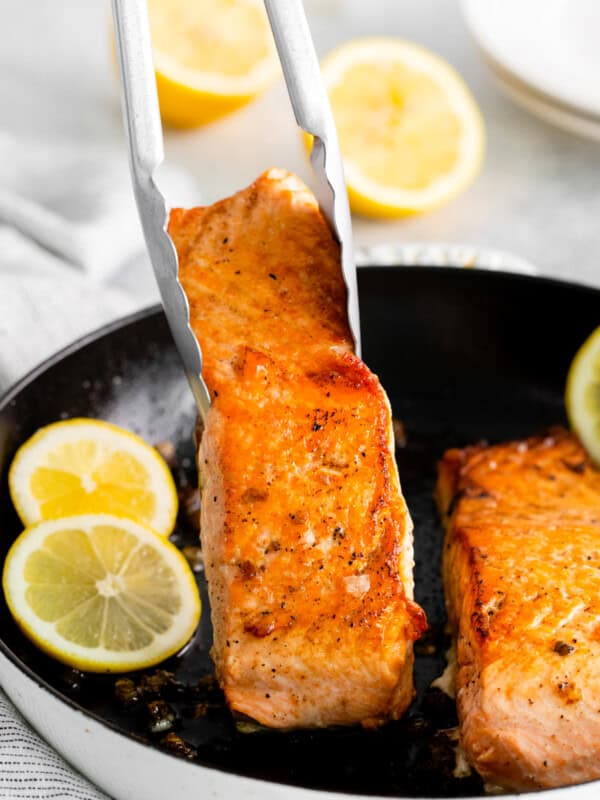 tongs grabbing a salmon filet from a cast iron pan.