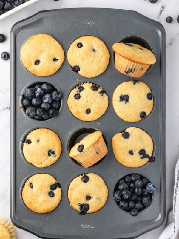 10 blueberry pancake muffins in a muffin tin with blueberries in the remaining muffin wells.