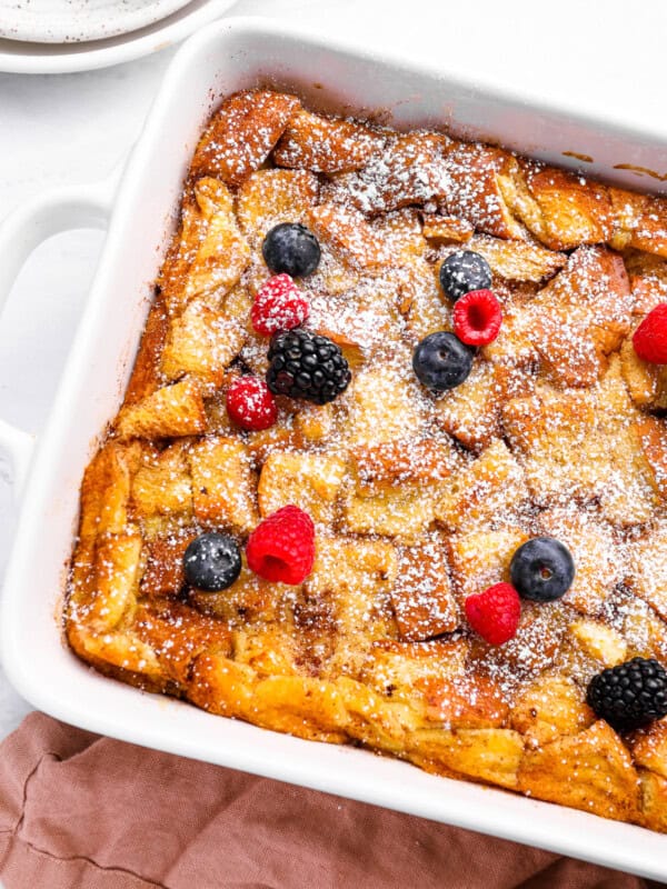 bread pudding in a white baking pan with powdered sugar and berries.