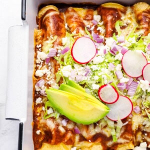 partial overhead view of chicken enchiladas topped with lettuce, radish, onion, and avocado.