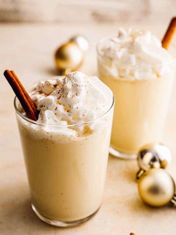 2 glasses of crockpot eggnog with whipped cream and cinnamon sticks.