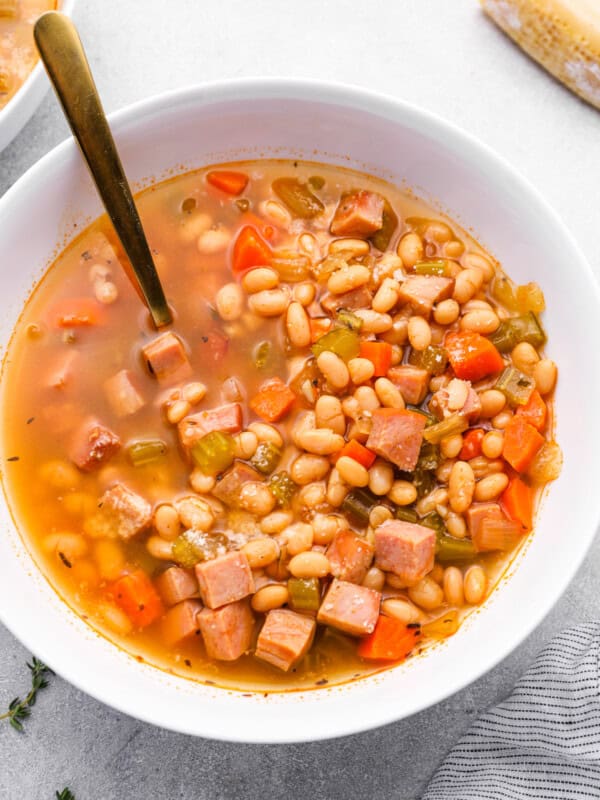 crockpot ham and bean soup in a white bowl with a spoon.