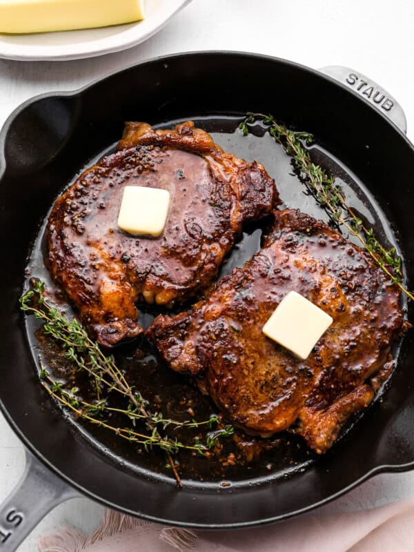 overhead view of oven baked steaks in a cast iron pan topped with a pat of butter and thyme.