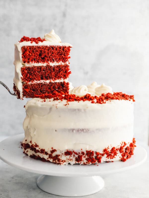 a cake server lifting a slice of red velvet cake from a cake on a white cake stand.