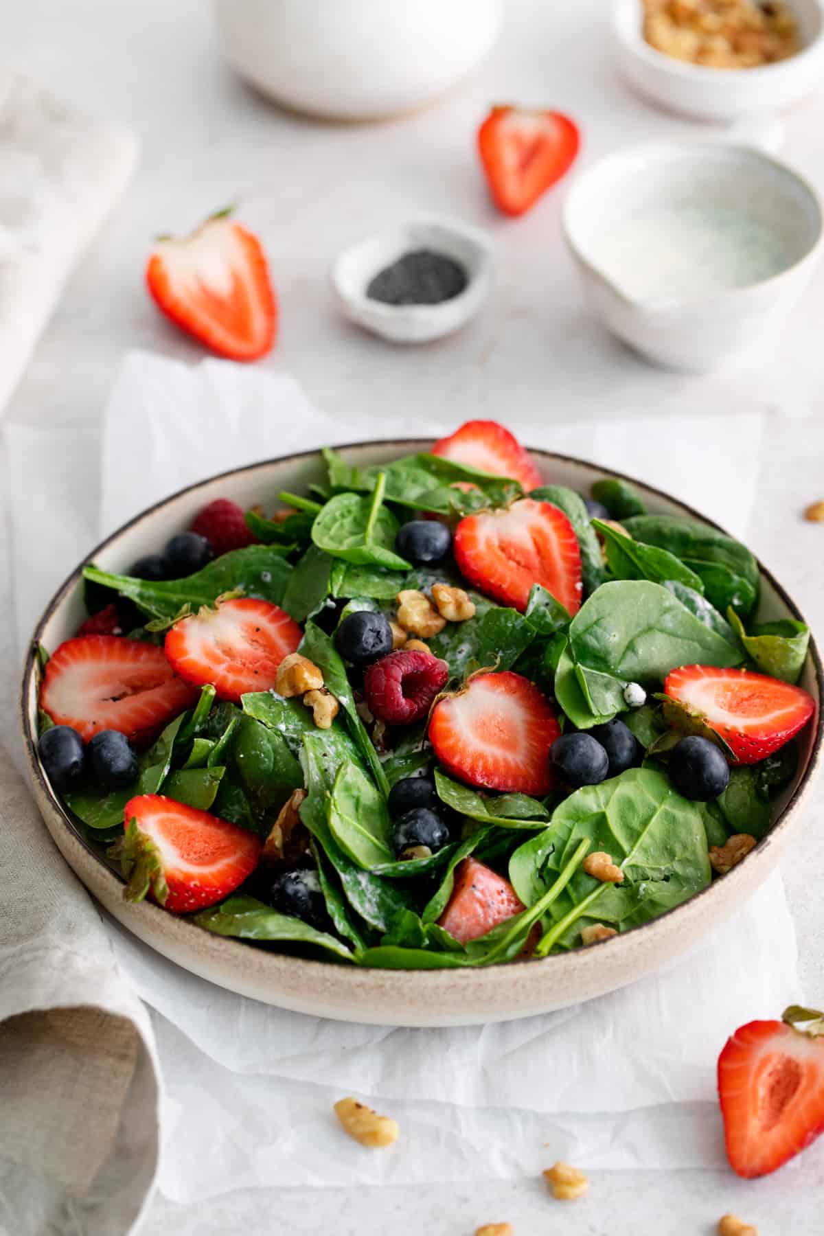 three-quarters view of spinach salad with mixed berries in a beige bowl.