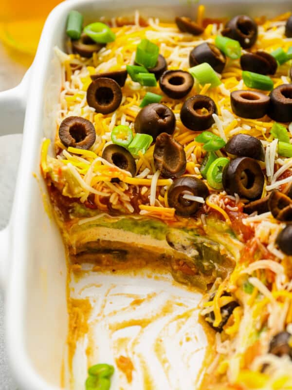 close up of partially eaten 7 layer dip in a rectangular baking pan.