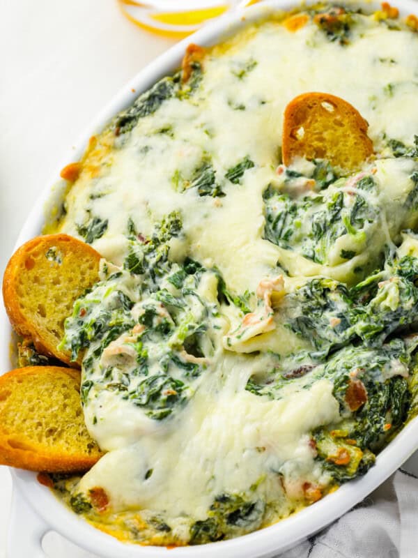 bacon spinach dip in an oval baking dish with toasted bread pieces stuck in.