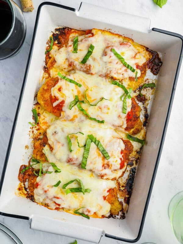 overhead view of chicken parmesan in a white rectangular baking pan topped with shredded basil.