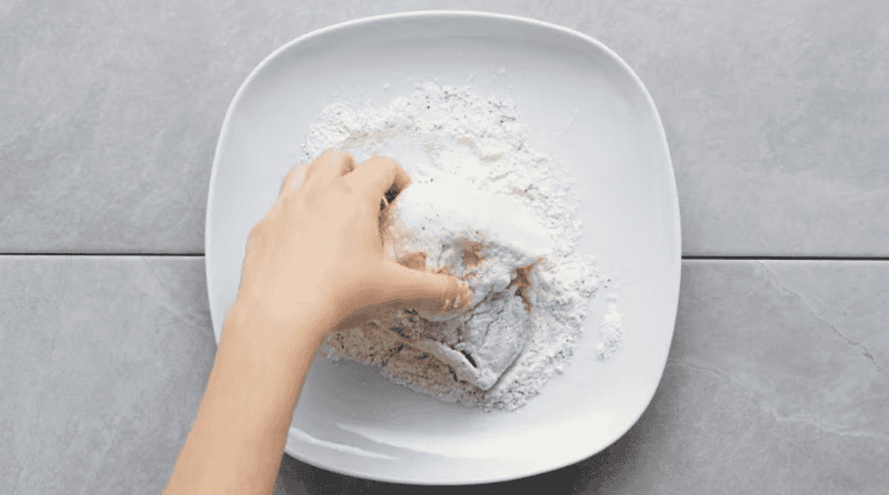 dredging a chicken thigh in seasoned flour.