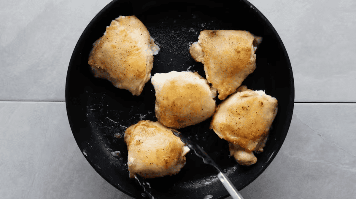 searing chicken thighs in a pan.