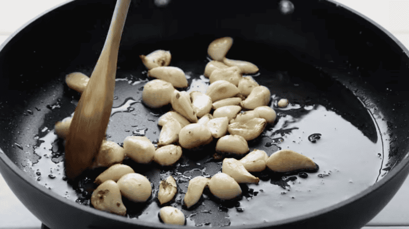 cooking whole cloves of garlic and herbs in a pan with a wooden spoon.