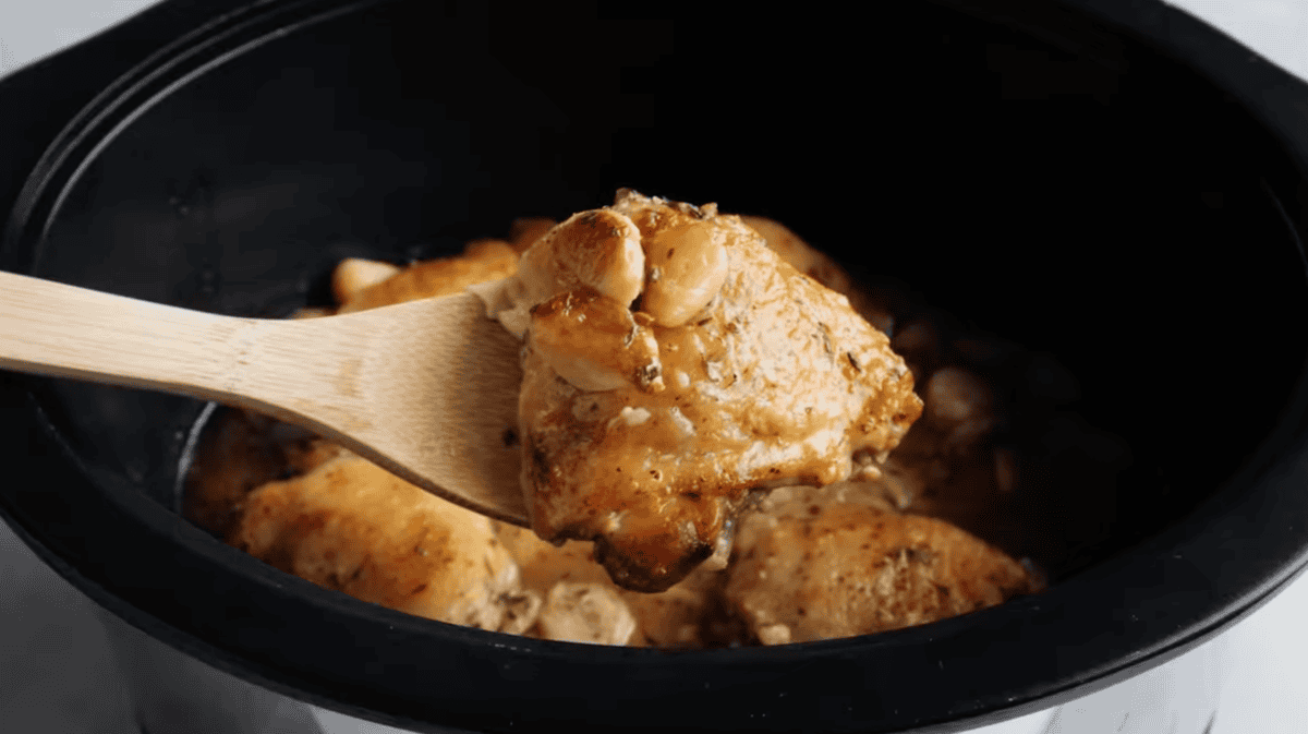 holding a cooked 40 clove garlic chicken thigh above a crockpot.