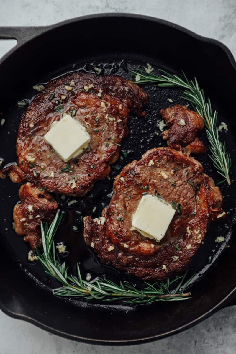 2 pan seared ribeye steaks in a cast iron pan with butter.