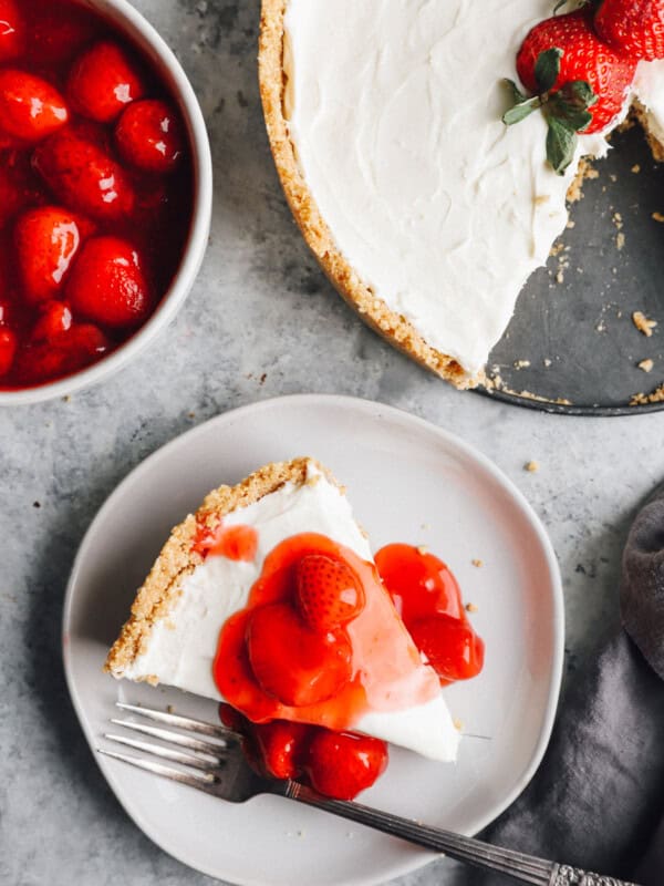 overhead view of a slice of no bake cheesecake on a white plate with strawberry topping and a fork.