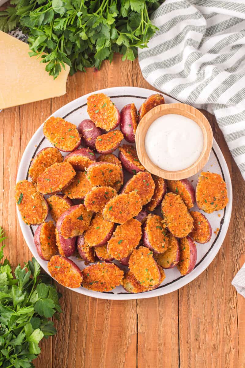 overhead view of parmesan roasted potatoes on a white serving platter with sour cream.