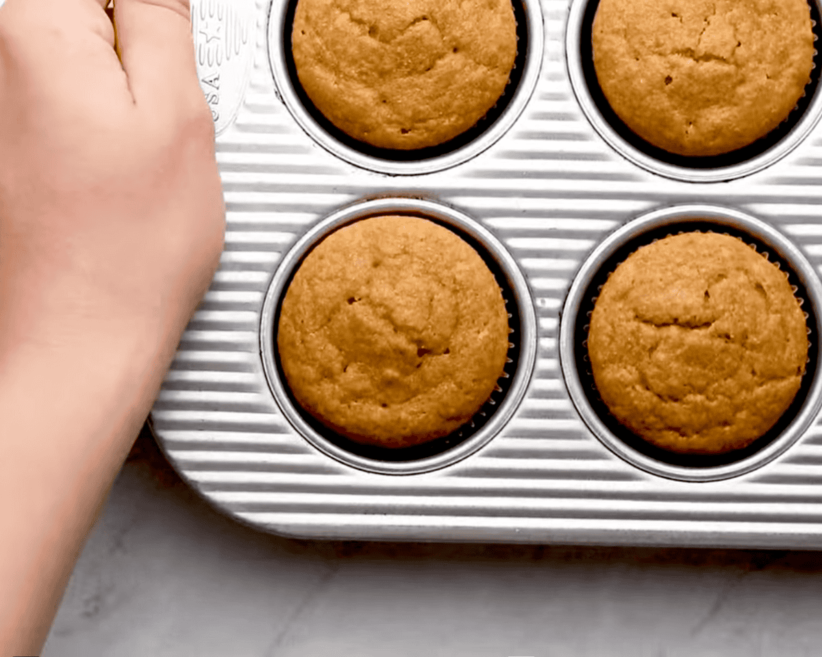 Fluffy baked dog cupcakes in a cupcake tin with a hand holding the side