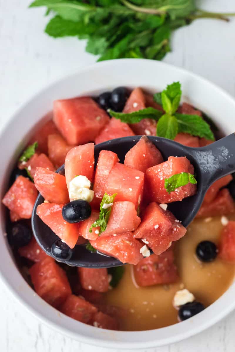 a spoon lifting watermelon salad from a white serving bowl.