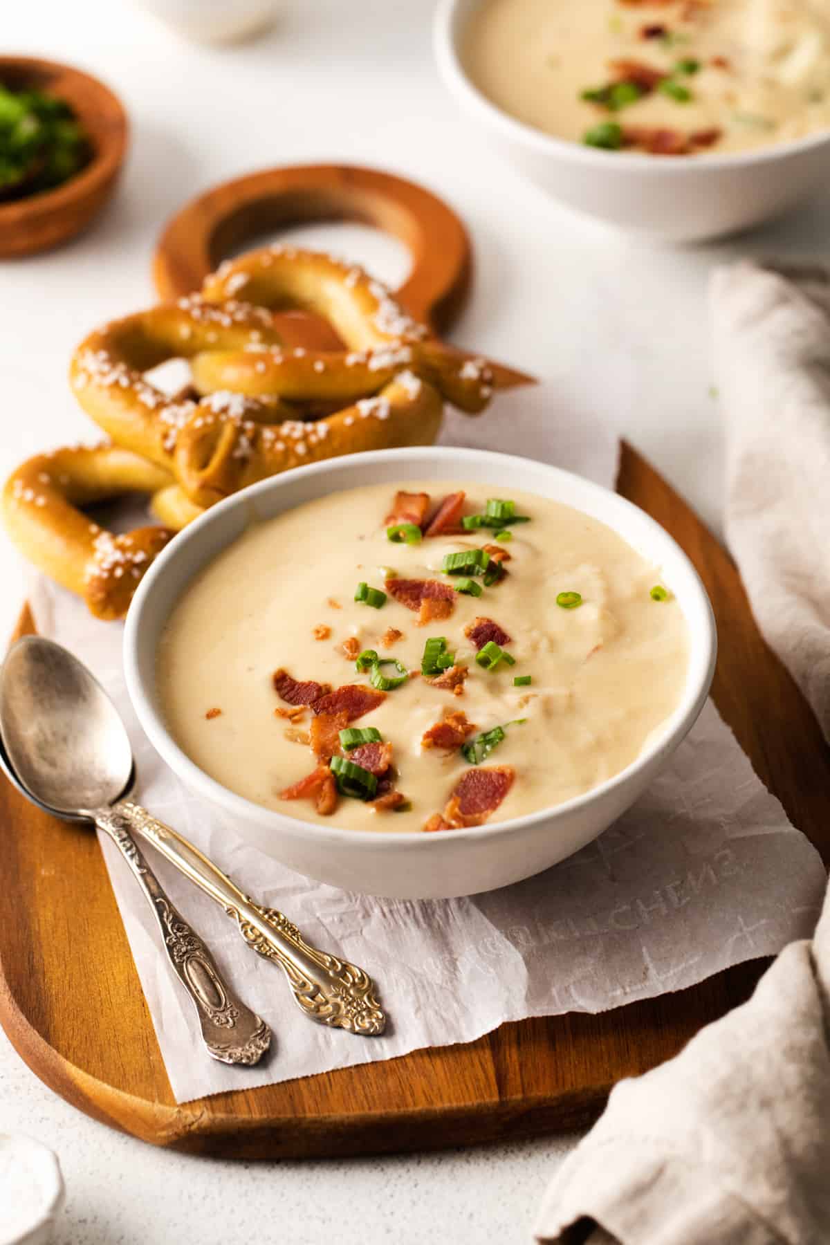 three-quarters view of a serving of beer cheese soup in a white bowl on a cutting board with 2 soft pretzels.