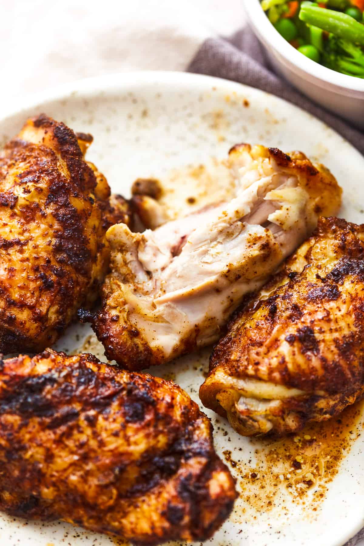 three-quarters view of 4 air fryer chicken thighs on a white plate, one is partially eaten.