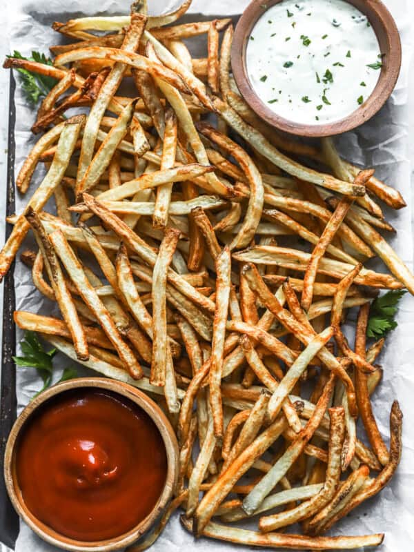 overhead view of air fryer french fries on a baking sheet with a cup of ketchup in the lower left corner and a cup of ranch in the upper right corner.