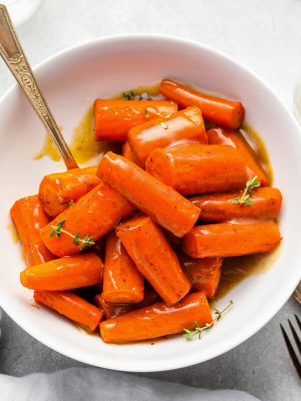 crockpot carrots in a white bowl with a serving spoon.