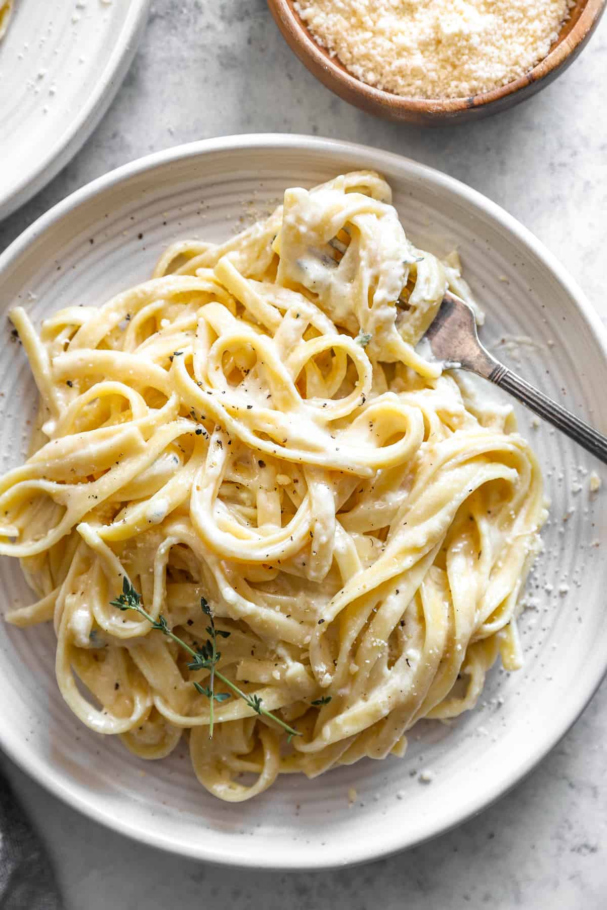 close up overhead view of a serving of fettuccini alfredo on a white plate with a fork.