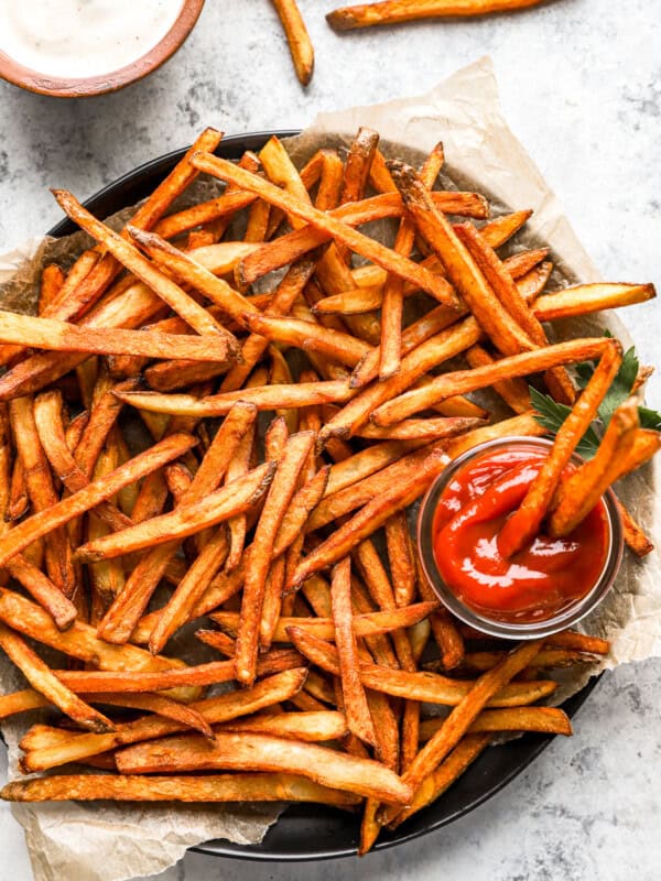 homemade french fries on a round serving tray with a cup of ketchup.