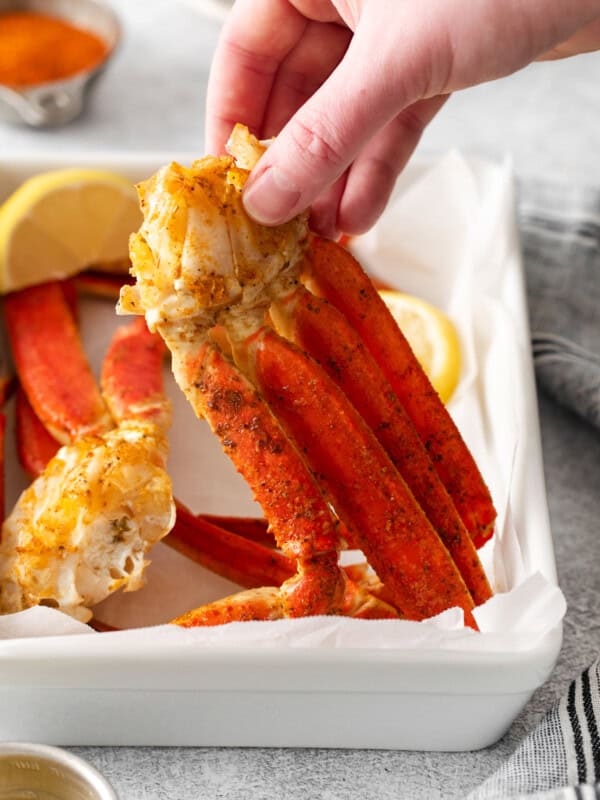 three-quarters view of a hand holding up a cluster of crab legs from a white rectangular plate.