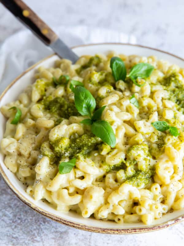 three-quarters view of a bowl of pesto mac and cheese with a fork.