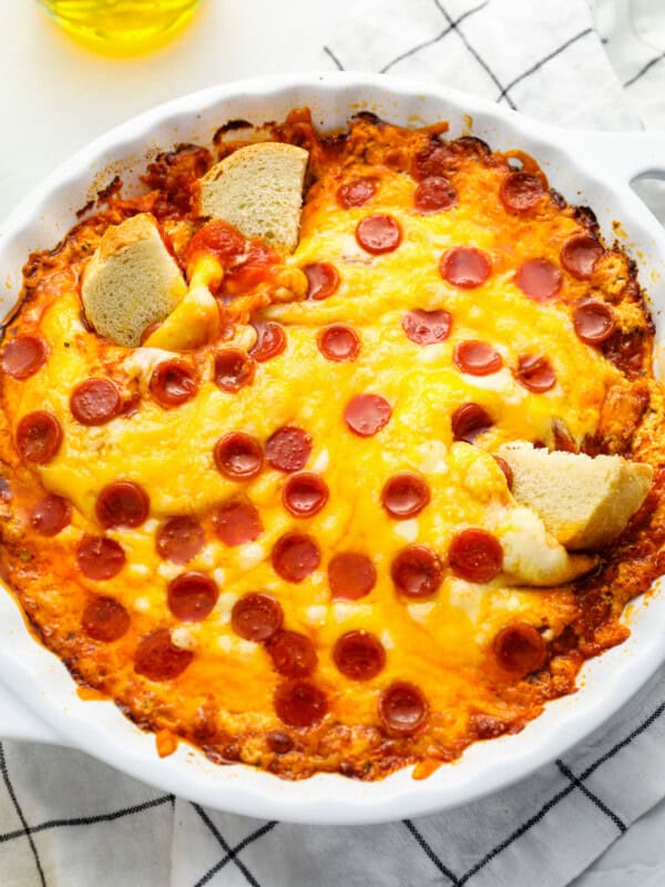 three-quarters view of pizza dip in a white round baking dish with 3 cubes of bread dipped in it.